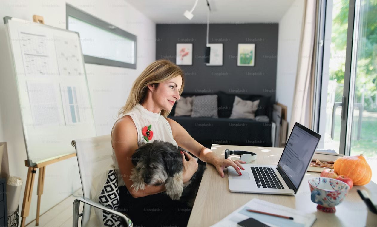 Woman working on laptop with a dog on her lap in a modern home office.