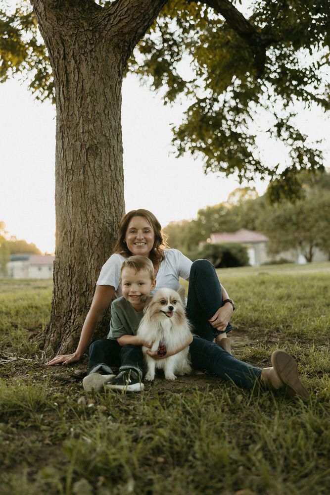 Woman sitting under a tree with her small dog on a leash during sunset.